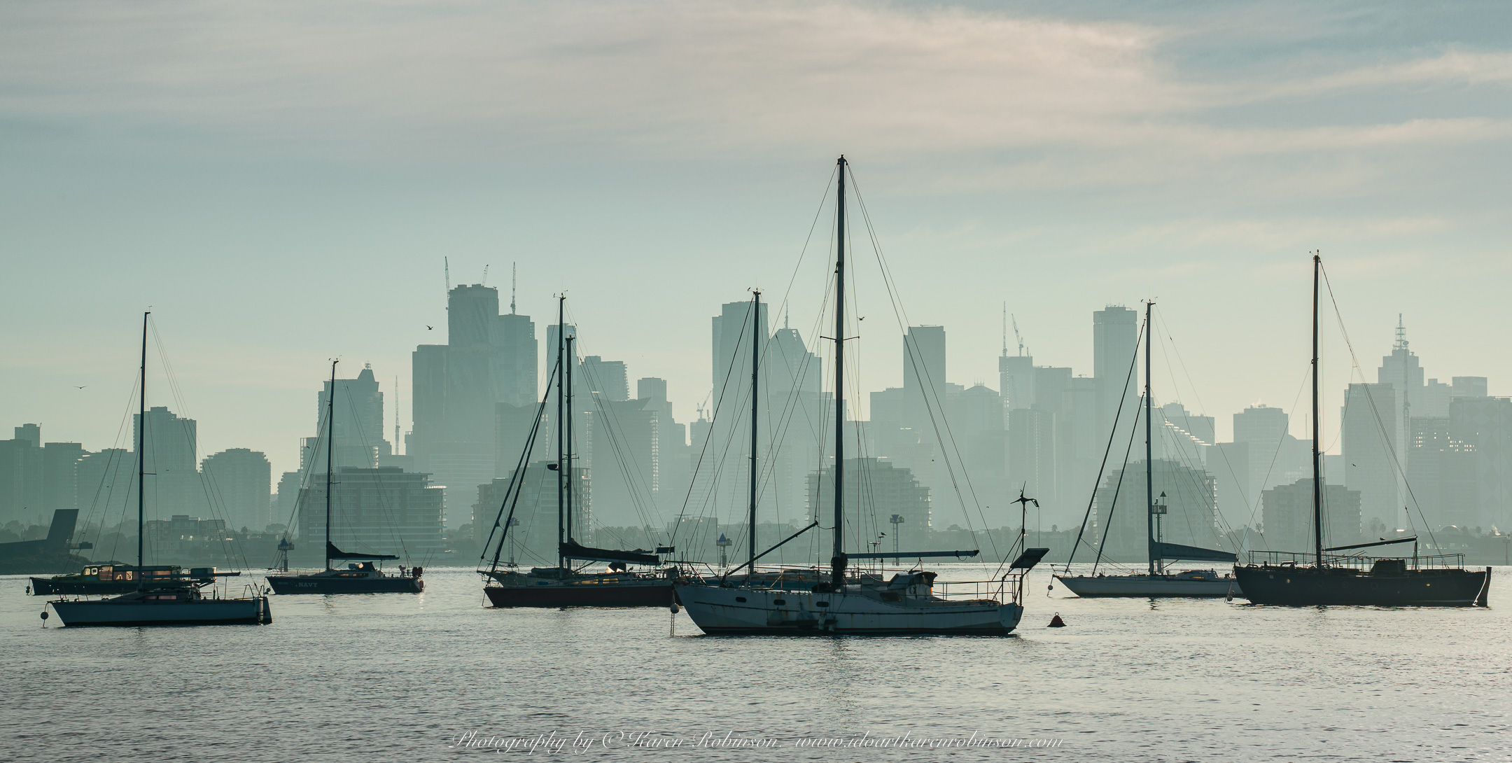 Williamstown, Victoria - Australia 'Views from Ferguson Street Pier' Photographed by ©Karen Robinson June 2022 Comment: Photograph featuring views across Port Phillip Bay towards Melbourne City Skyline and anchored boats and yachts.